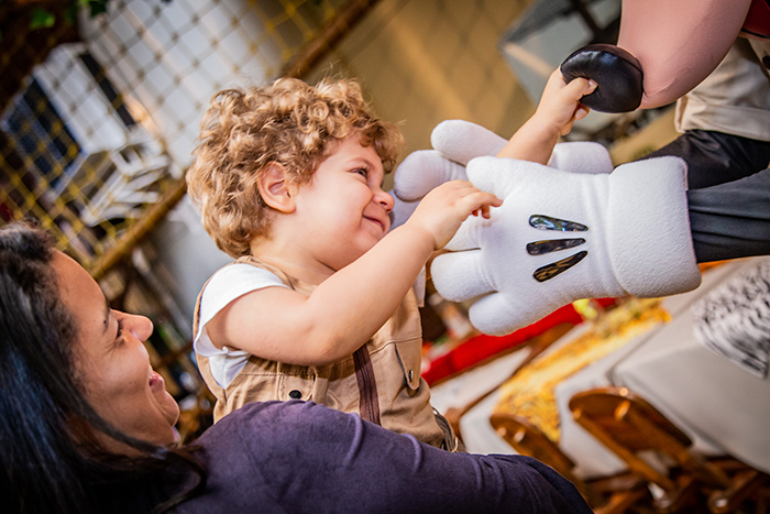 Menino no colo brincando e sorrindo, apertando nariz do Mickey
