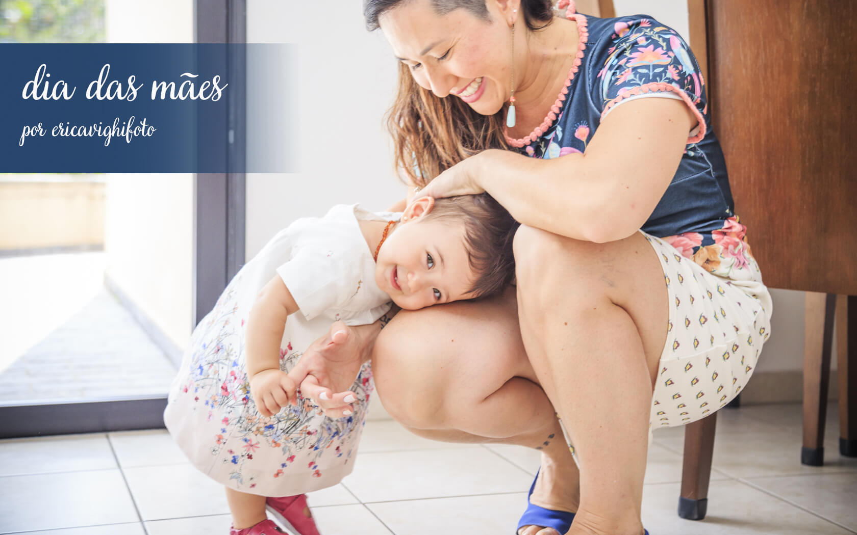 mamãe ajoelhada, e bebê em pê, com a cabecinha apoiada em seu joelho. Ambas sorrindo