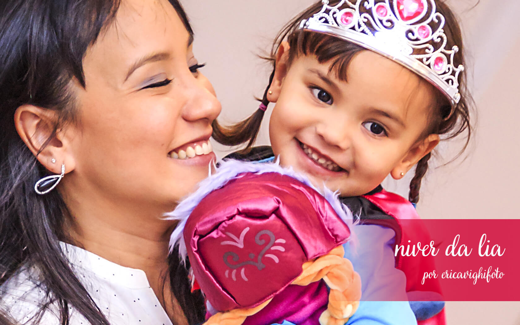 mamãe sorrindo com a lia, vestida de ana, no colo, sorrindo também.